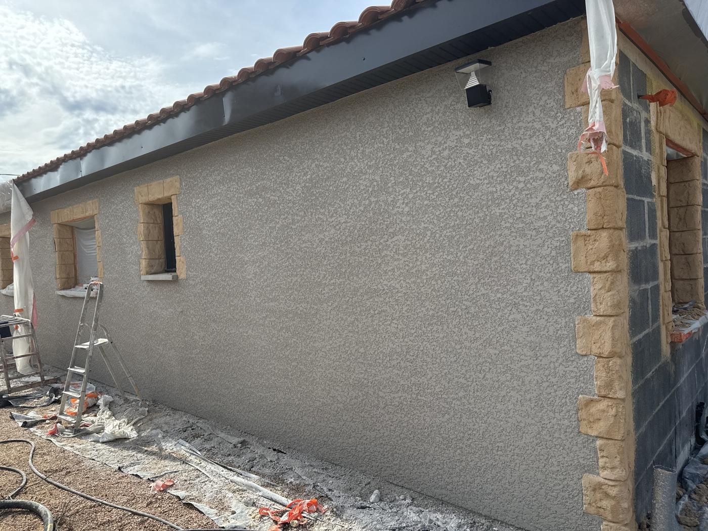 Mur à l'enduit gris en finition rustique, encadrements façon pierre en cours de pose